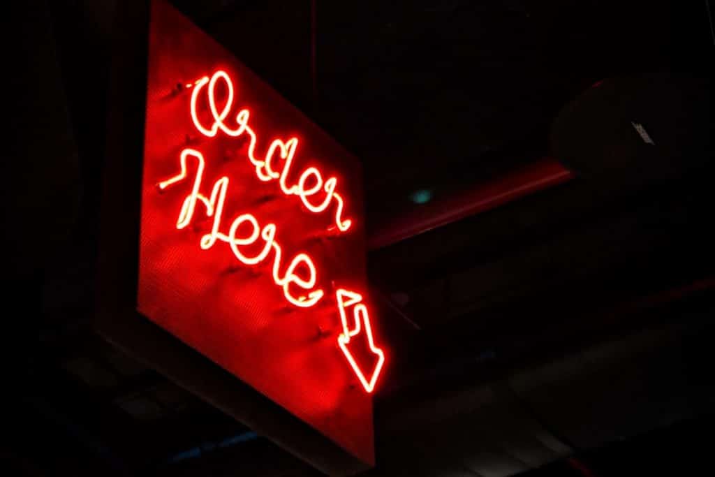 A neon light at night with Order Here being the text