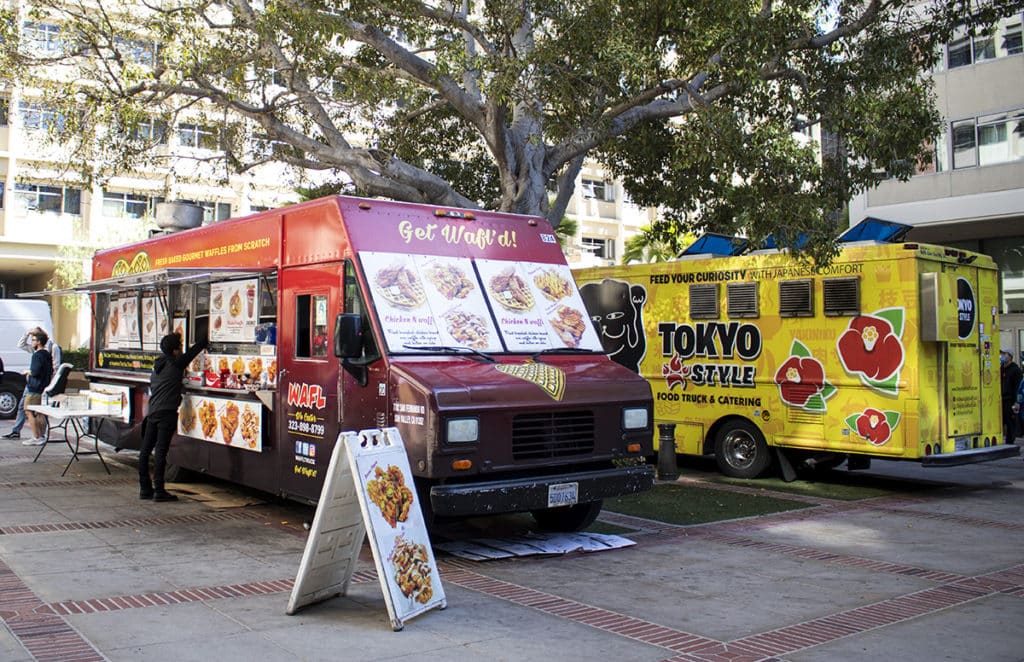 Two food trucks serving asian cuisine parked under trees by ucla