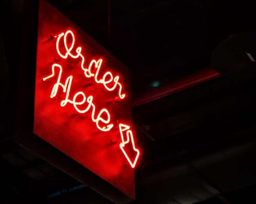A neon light at night with Order Here being the text