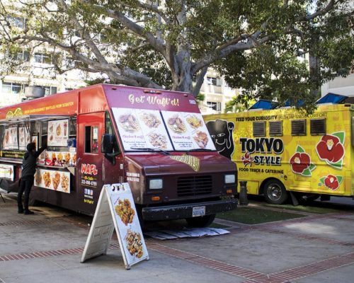 Two food trucks serving asian cuisine parked under trees by ucla